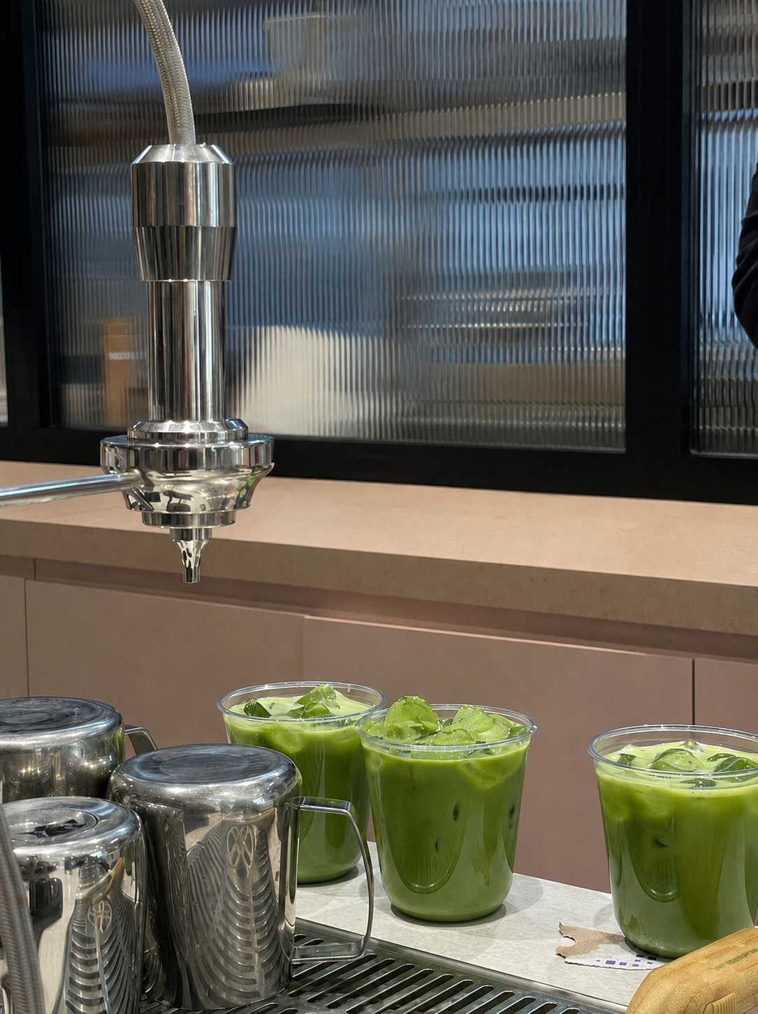 Iced matcha lattes lined up on a café counter next to milk pitchers